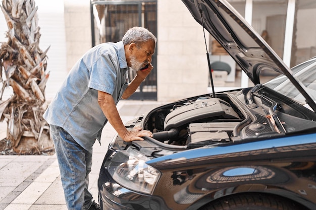 Senior greyhaired man talking with insurance for car engine problem at street