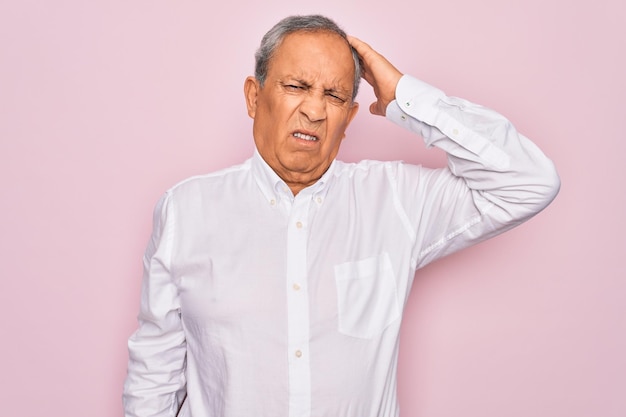 Senior handsome greyhaired man wearing elegant shirt over isolated pink background confuse and wonder about question Uncertain with doubt thinking with hand on head Pensive concept