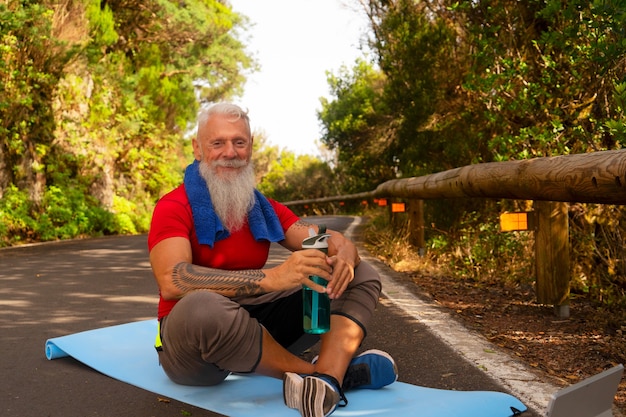 Senior happy smiling man with white beard resting while doing exercises outdoor on the nature