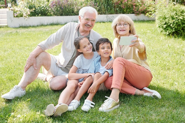 Senior lady taking selfie of herself, her husband and grandchildren on smartphone camera