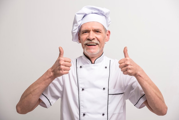 Senior male chief cook in uniform showing thumb up.