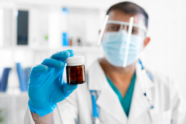 Senior male doctor in mask holding glass jar with medicine