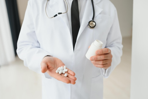 Senior male doctor with stethoscope in medical scrubs and holding bottle and tablets