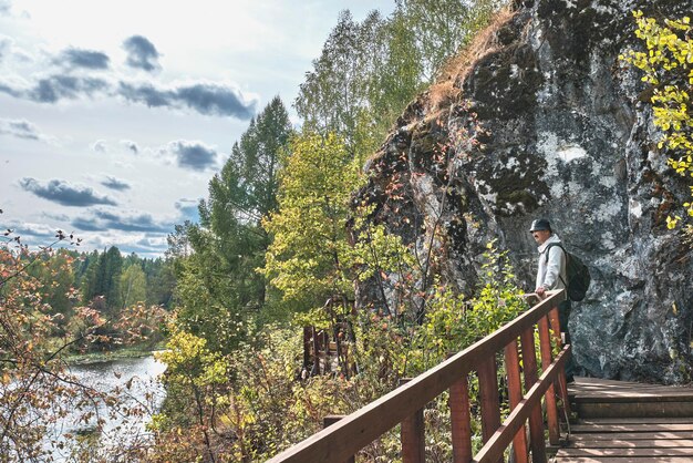 Senior male hiker admiring landscape with river on wooden hiking trail near cliff Nature park