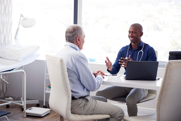 Senior Male Patient In Consultation With Doctor Sitting At Desk In Office