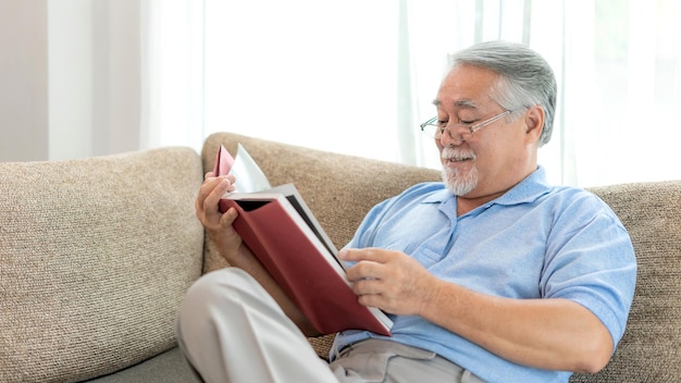 Senior Male reading novel book smiling feel happy on sofa at home lifestyle senior elderly people concept