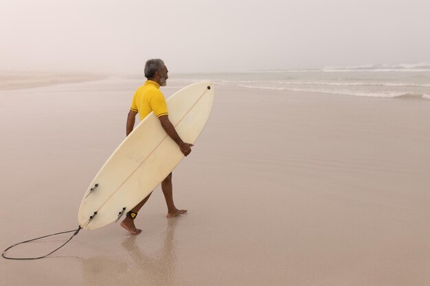 Photo senior male surfer walking with surfboard on the beach