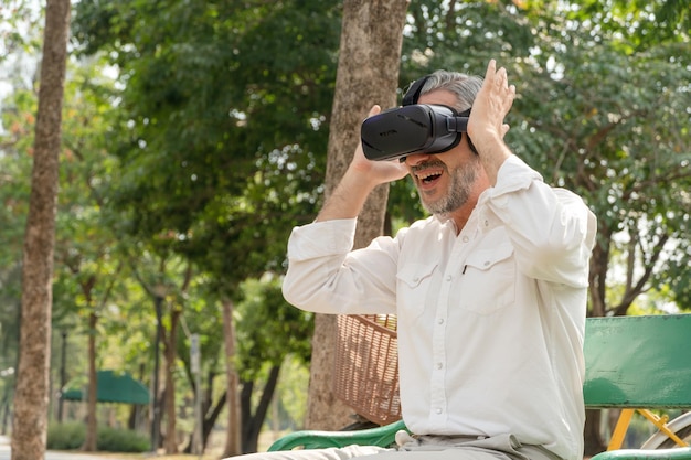 Senior man excited watching on VR glasses sitting at park