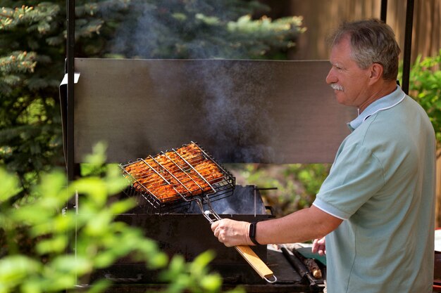 Photo senior man grilling in the backyard of his country house in sunny summer day