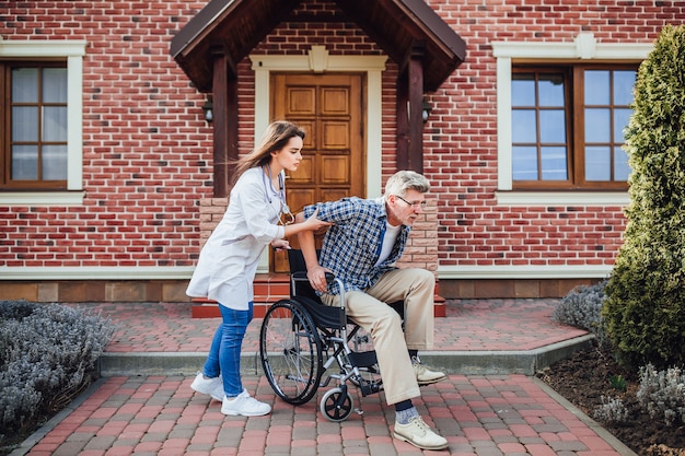 Senior man happiness sitting on wheelchair with smiling nurse, takes care and discussion and cheer in the garden at nursing home 