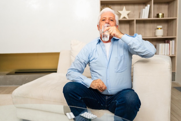 Senior man holding glass drinking fresh water at home mature old senior thirsty grandfather takes