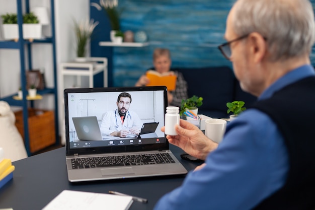 Senior man listening doctor during telemedicine holding pills bottle