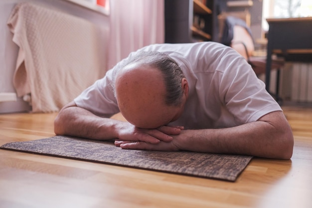 Senior man meditating on a wooden floor and lying in Shavasana pose