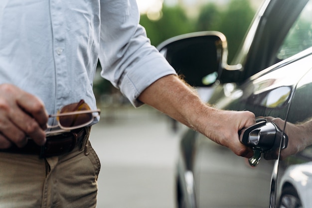 The senior man opens the door of his car with keyless access. Hand on the door handle close up.