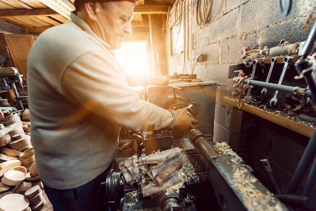 A senior man procesing wood on a lathe and making wooden dishes in the workshop.