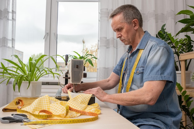 Senior man seamstress sitting and sews on sewing machine in studio Concept of Factory