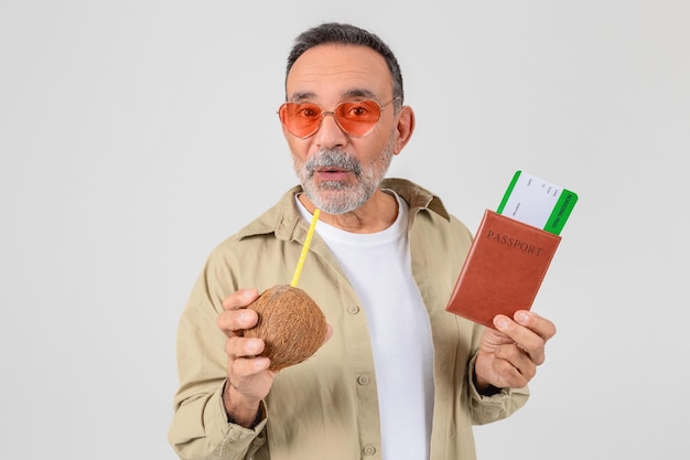 Senior man sipping drink with passport and boarding pass