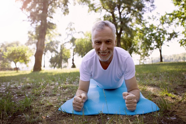 Senior man smiling broadly and keeping his arms on ground pad while training outdoors