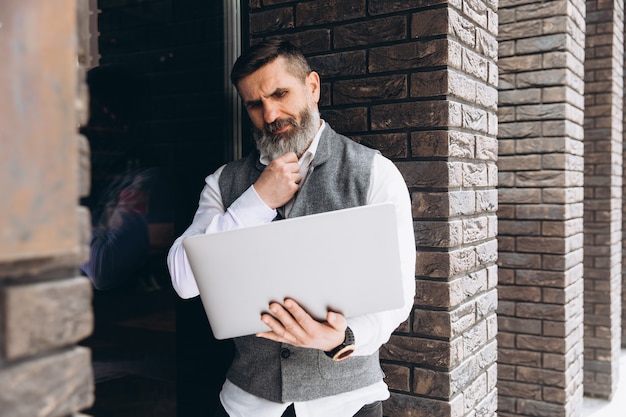 Senior man stylish man with gray beard spends time outdoors in laptop