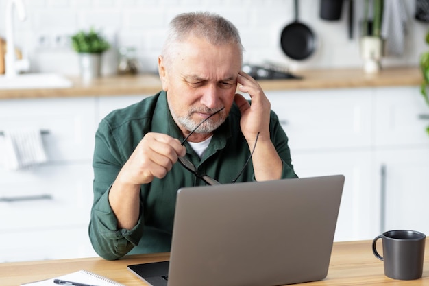 Senior man suffering from severe headache while working on laptop