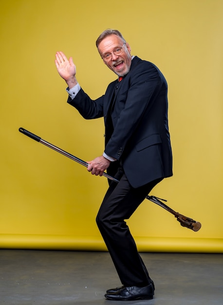 Senior man in suit sitting on a boom. Manager man playing funny games with a mop in studio.