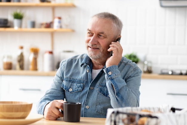 Senior man talking on phone sitting at the table at home