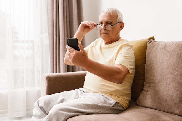 Senior man wearing eyeglasses is using smartphone