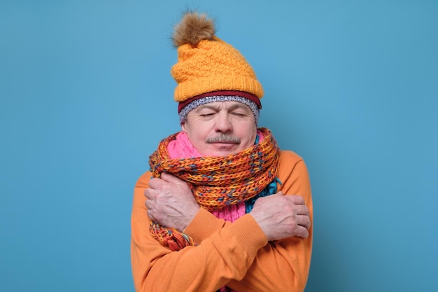 Senior man wearing several hats and scarfs freezing because of cold weather