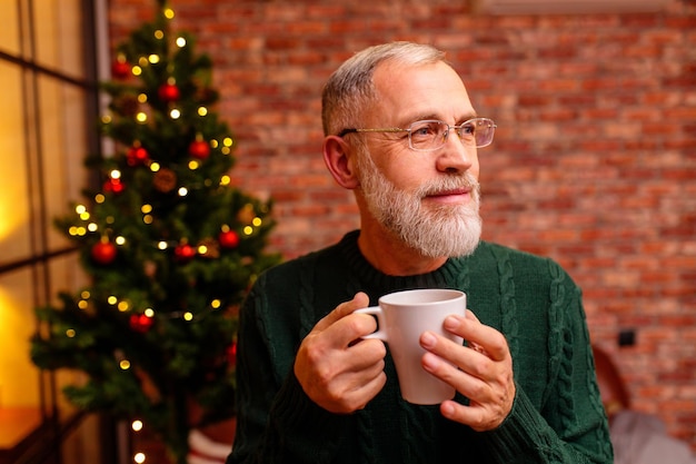 Senior man with a cup sitting at home near Christmas tree