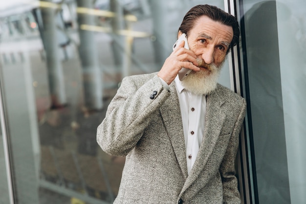 Senior man with a gray beard and mustache in a jacket talks on the phone