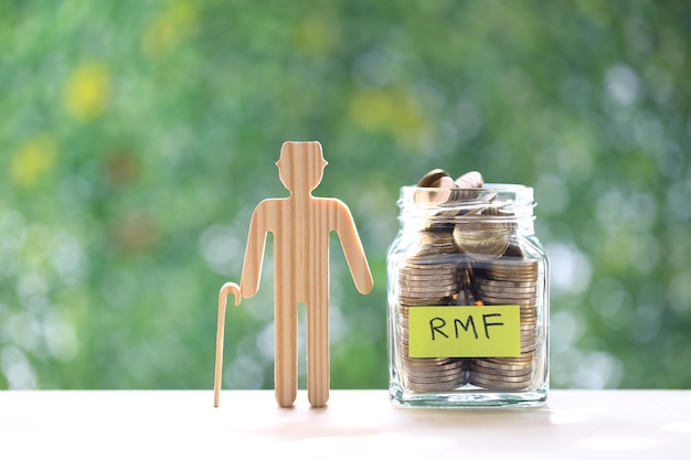 Senior man with RMF word and stack of coins money in glass bottle on natural green background