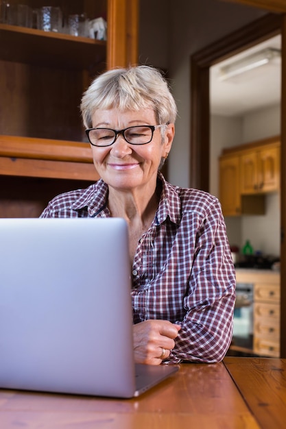 Senior mature woman using laptop at home watching online webinar