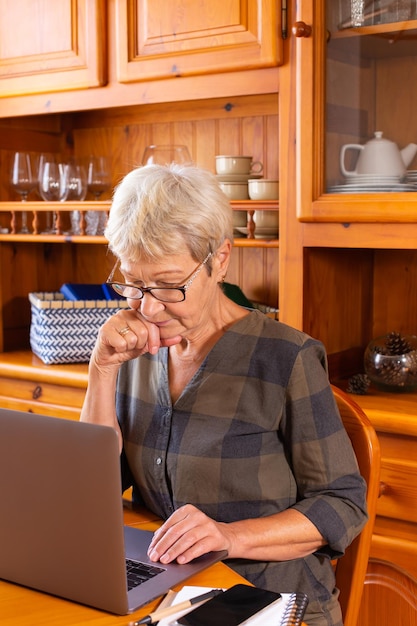 Senior mature woman using laptop at home watching online webinar