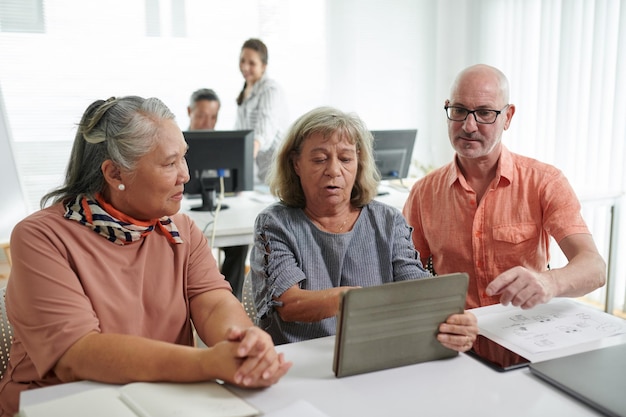 Senior men and women discussing how to install application on digital tablet