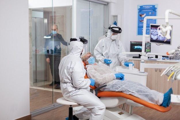 Senior patient wearing hazmat suit during coronavirus in dentist office Elderly woman in protective uniform during medical examination in dental clinic