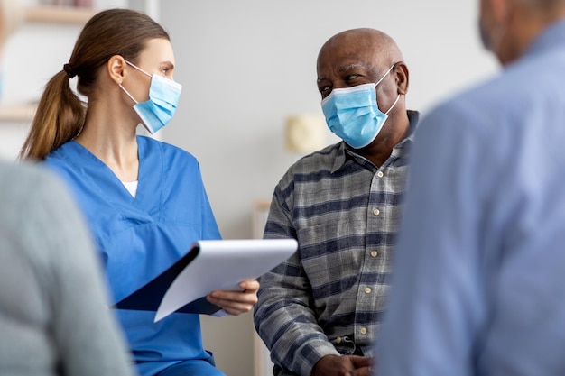 Senior patients in face masks having conversation with nurse