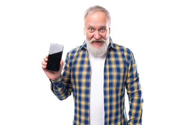 Senior pensioner grayhaired man with a beard in a shirt holds a smartphone with a mockup on a white