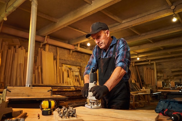 Senior Professional carpenter in uniform working of manual milling machine in the carpentry workshop