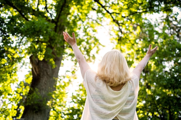 Senior scandinavian woman by the tree holding hands up