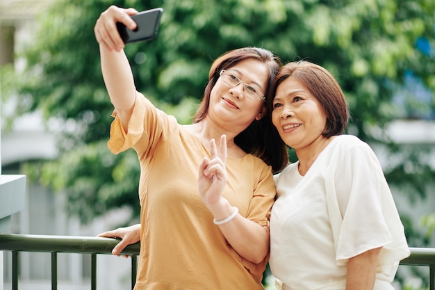 Senior smiling Asian women taking selfie on smartphone when standing outdoors