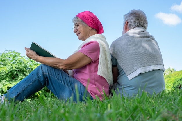 Senior smiling couple sitting on the grass in public park having relaxed moments Romantic couple enjoying free time and retirement