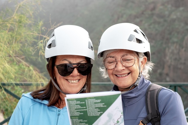 Senior smiling women hikers with helmets standing on the top of mountain looking at map