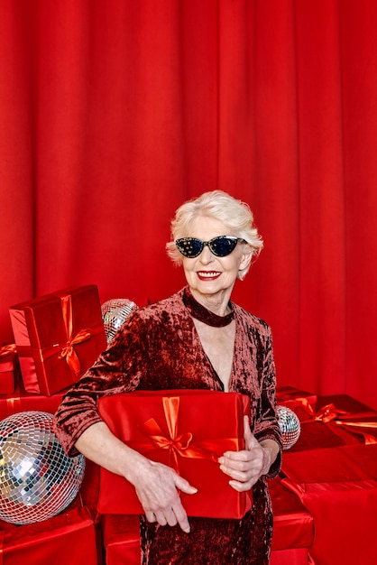 senior stylish woman with presents on red background. Party, fashion, celebration, anti age concept