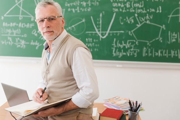 Senior teacher sitting on desk and writing in notebook