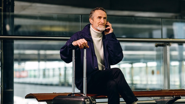 Photo senior tourist sitting at airport terminal and talking on cell phone