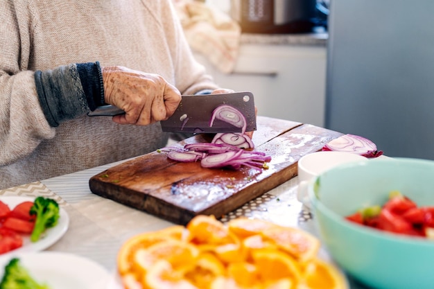 Senior vegan woman cutting onion and preparing salad on wooden cutting boardx9