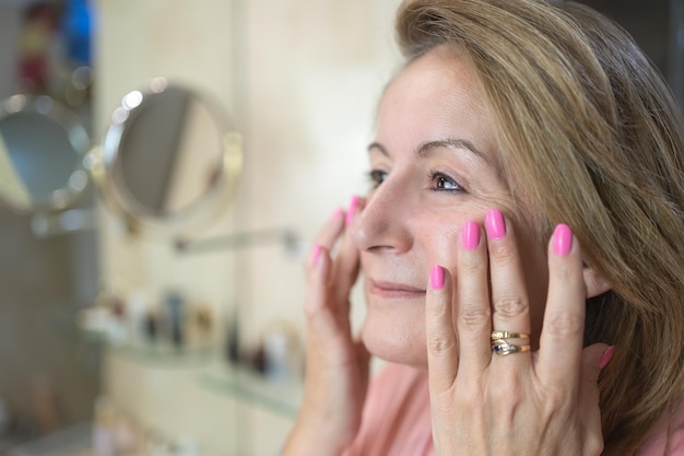 Senior white woman applying moisturizer for skin care on her face