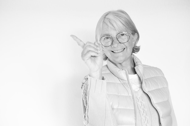 Senior whitehaired woman smiling and looking at the camera pointing with hand and finger to the side