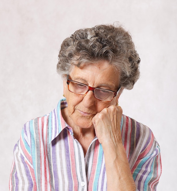 Senior woman between 70 and 80 years old is thinking about something. Gray  background