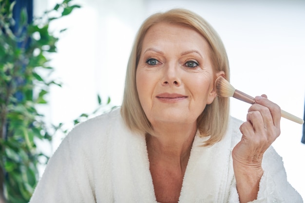 senior woman applying makeup in the bathroom